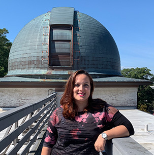 An image of Valentina Missaglia on the walkway in front of a ground-based observatory on a sunny day.