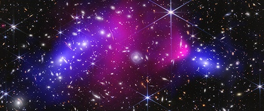 Webb near-infrared data combined with Chandra X-ray data of the Bullet Cluster show many overlapping objects, including foreground stars, galaxies in galaxy clusters, and distorted background galaxies behind the galaxy clusters. The objects are all at various distances set against the black background of space. Most galaxies appear as tiny fuzzy ovals in white, orange, or red. A slightly larger, very bright, light blue spiral galaxy is at center. To its immediate left and right are two large bright pink splotches representing X-rays. The right pink area has a rounded nose facing right, where it is darker pink, and fades to the left as a triangular shape. This is referred to as the Bullet. To the far left and far right, next to the pink regions, are two blue regions representing dark matter mass. The left blue region is a large, long oval at an angle. The blue region at right is a far smaller oval.